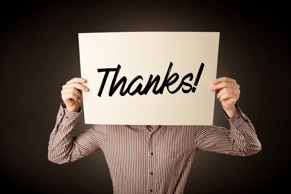 Young businessman hiding behind an expression of gratitude drawn on paper